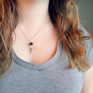 Puede incluir: Un collar de cadena de plata con una pequeña cuenta de lava negra y un colgante de pluma de plata.
