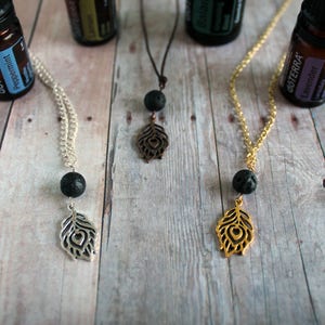 May include: Three silver, gold, and brown lava stone necklaces with a peacock feather pendant. Each necklace has a black lava stone bead and a silver, gold, or brown peacock feather pendant.