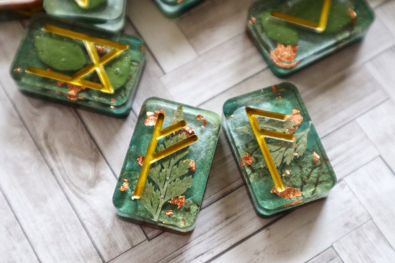 May include: Set of five green resin rune stones with gold leaf and gold foil accents. Each stone features a different rune symbol.