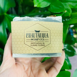 Peut inclure: Un savon artisanal naturel de Chautauqua Soap Co. de couleur grise avec une étiquette brune sur laquelle est écrit "Chautauqua Soap Co. Savon artisanal naturel Patchouli & Ylang Ylang"