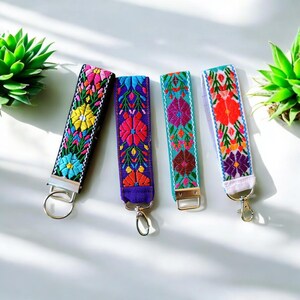 May include: Four colorful keychains with embroidered floral patterns. The keychains are made of fabric and have silver metal key rings.