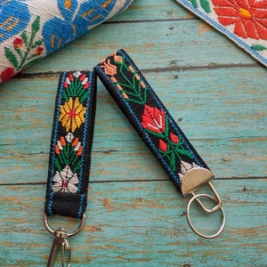 May include: Two black keychains with silver key rings. Each keychain has a colorful embroidered floral design with red, orange, yellow, green, blue, and white thread.