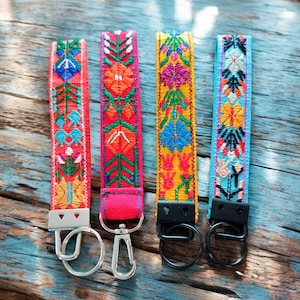 May include: Four colorful keychains with embroidered floral patterns. Each keychain has a silver or black metal ring attached.