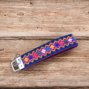 May include: A colorful key chain with a blue base and a geometric pattern in pink, yellow, green, and white. The key chain has a silver key ring.