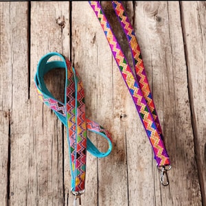 May include: Two colorful patterned lanyards with metal clasps. The lanyard on the left is blue with pink, orange, yellow, and green accents. The lanyard on the right is purple with orange, yellow, and green accents.
