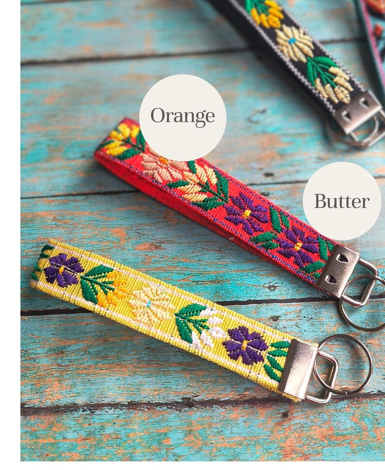 May include: Three fabric keychains featuring embroidered floral patterns in yellow, red, and black. Each strap is finished with a silver-toned metal clamp and a circular split ring. The text labels Orange and Butter are visible on the image.