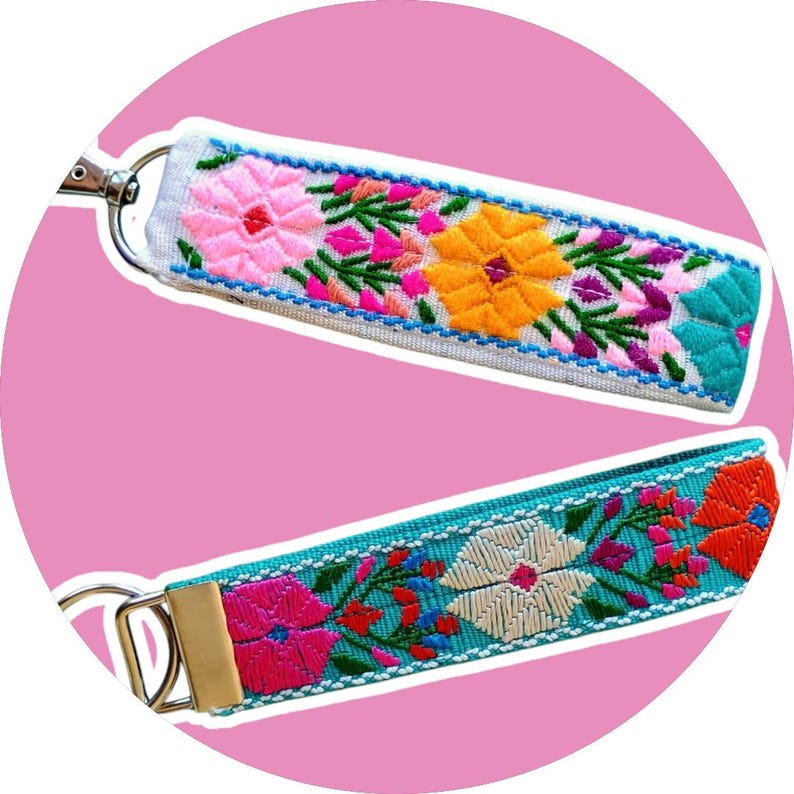 May include: Two colorful embroidered keychains with floral designs. One keychain is white with turquoise accents and the other is turquoise with white accents.