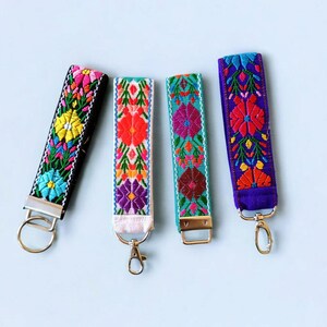May include: Four colorful embroidered keychains with floral patterns. The keychains are black, white, turquoise, and purple. Each keychain has a silver key ring.