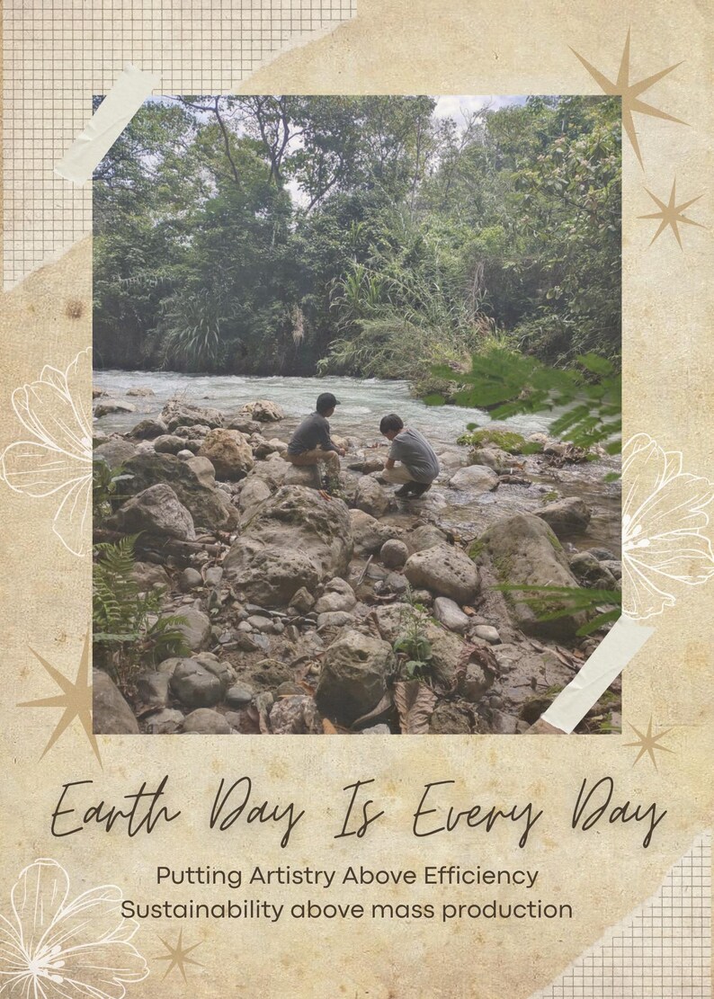 May include: A rectangular graphic print featuring a photograph of two individuals sitting on rocks by a flowing river surrounded by trees. The text reads Earth Day Is Every Day, Putting Artistry Above Efficiency, Sustainability above mass production.