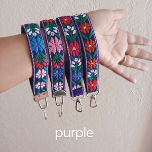 May include: Four purple fabric wristlet keychains featuring a woven floral pattern in shades of red, pink, blue, green, and white. Each strap is finished with a silver-toned metal clasp and a circular split ring for attaching keys or accessories.