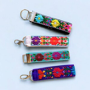 May include: Four colorful embroidered keychains with different floral patterns. The keychains are on a light blue background.