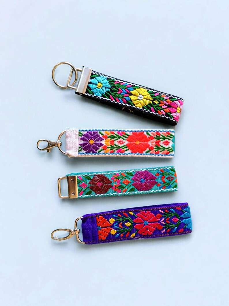 May include: Four colorful embroidered keychains with different floral patterns. The keychains are on a light blue background.