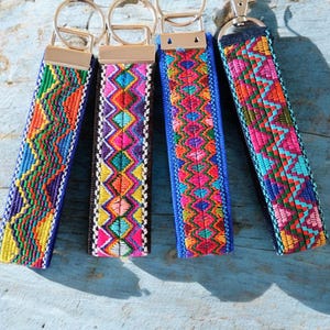 May include: Four colorful keychains with geometric patterns. Each keychain has a silver key ring and a blue strap with a colorful woven design.