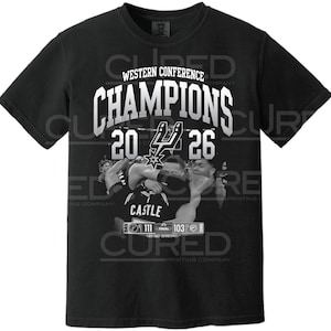 Puede incluir: Una camiseta negra de manga corta con el texto blanco WESTERN CONFERENCE CHAMPIONS 20 26 y el logotipo de los San Antonio Spurs en el centro. Debajo del texto hay un gráfico de jugadores celebrando y un marcador con un resultado final de 111 a 103.