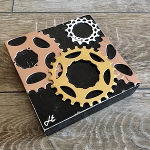 Bicycle inspired wall art sculpture created by artist Jon Edmondo using bike chain rings and gears. Titled Gold, Silver and Bronze.