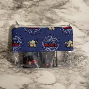 May include: A blue zippered pouch with a clear plastic front. The pouch has a repeating pattern of a cartoon character from Star Wars: The Mandalorian, the words "Star Wars", and stars. The clear front shows a Disneyland ticket for Star Wars: Galaxy's Edge.
