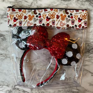 May include: A clear zipped pouch containing a pair of black and white polka dot mouse ears with a red sequined bow. The top of the pouch has a white fabric border with a food-themed pattern, including pizza, pretzels, and Mickey Mouse.