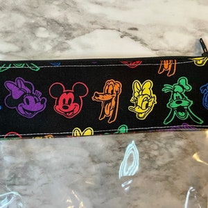 May include: A clear pencil case with a black top featuring colorful cartoon character faces. The characters include Mickey Mouse, Minnie Mouse, Donald Duck, and Goofy. The pencil case has a black zipper.