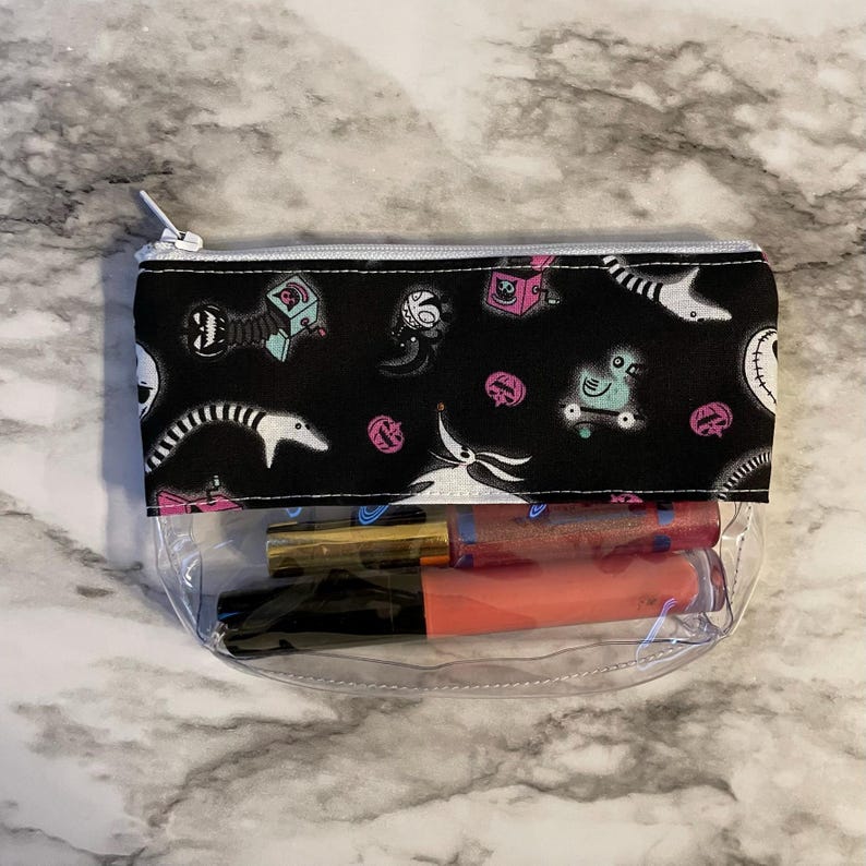 May include: A clear zippered pouch with a black fabric lining featuring a repeating pattern of characters from the Nightmare Before Christmas. The pouch is filled with two lip glosses.