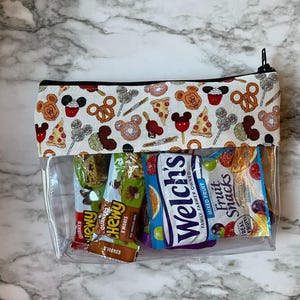 May include: A clear, zippered pouch containing snacks. The top band has a white background with a pattern of Mickey Mouse-themed treats. Inside are snack bars and Welch's Fruit Snacks.