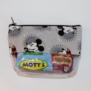 May include: A grey zippered pouch with a Mickey Mouse print. The pouch is clear and contains a Mott's fruit snacks packet.