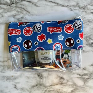 May include: A clear plastic zippered pouch with a blue fabric lining featuring a repeated pattern of Spider-Man characters and the text "Let's Go Spidey Team!" The pouch contains a small bottle of hand sanitizer and a card with a cartoon character.