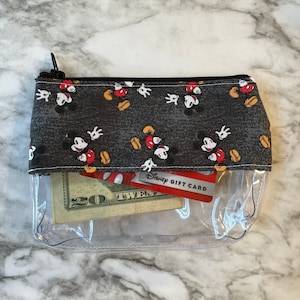 May include: Clear plastic zippered pouch with a black fabric lining featuring a repeating pattern of Mickey Mouse heads. The pouch contains a twenty dollar bill and a Disney gift card.