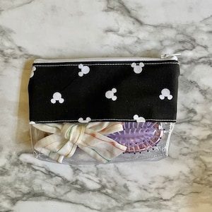 Pu&ograve; includere: Una pochette trasparente con cerniera, con una fodera in tessuto nero con un motivo di Topolino bianco. La pochette contiene un nastro a righe bianche e rosa e una spazzola per capelli viola.
