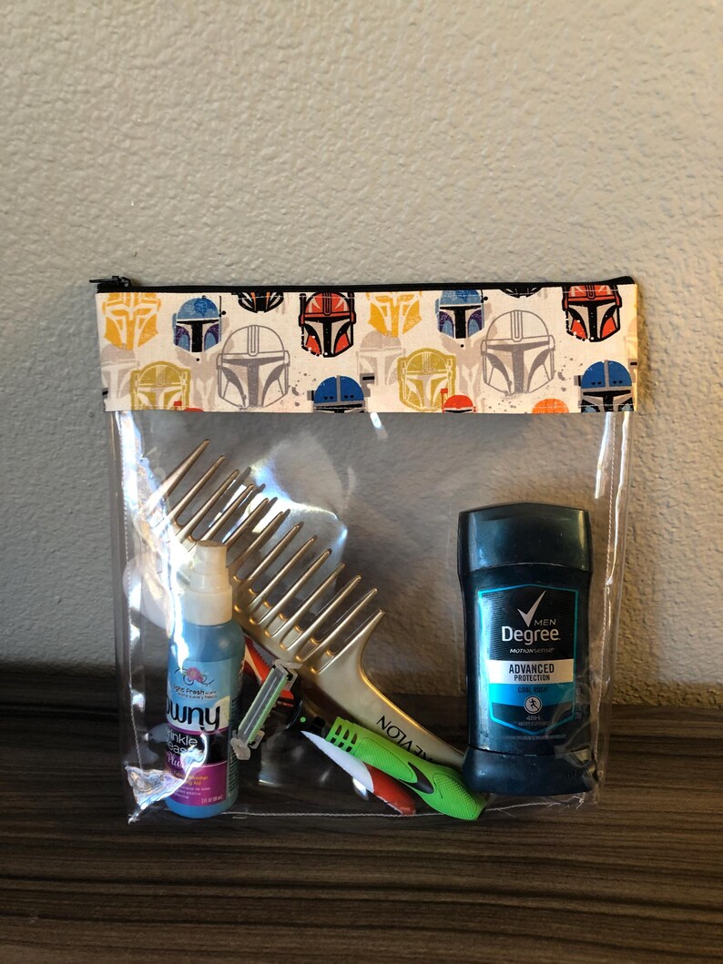 Puede incluir: Una bolsa transparente de pl&aacute;stico con cremallera negra y una solapa de tela estampada. La bolsa contiene un peine dorado, una botella azul de spray, una maquinilla de afeitar verde y roja y un desodorante azul en barra con el texto "MEN Degree ADVANCED PROTECTION" en la etiqueta.