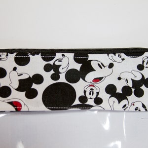 K&ouml;nnte beinhalten: Eine transparente, rechteckige Tasche mit einem schwarzen Rei&szlig;verschluss und einer wei&szlig;en Stoffoberseite. Der Stoff ist mit schwarz-wei&szlig;en Mickey Mouse-Gesichtern und Tupfen gemustert. Die Tasche ist wahrscheinlich zur Aufbewahrung.