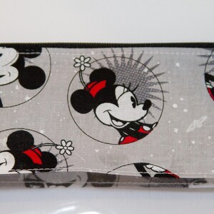 May include: A grey zippered pouch with a repeating pattern of Mickey Mouse and Minnie Mouse in black and white with red accents. The background is a light grey with white speckles.