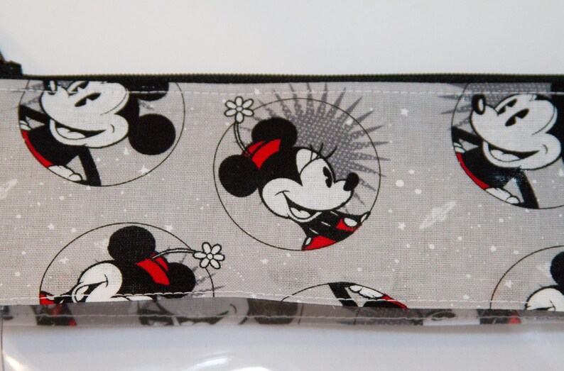 May include: A grey zippered pouch with a repeating pattern of Mickey Mouse and Minnie Mouse in black and white with red accents. The background is a light grey with white speckles.