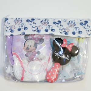 May include: A clear plastic zippered pouch with a white fabric flap featuring a blue and white Mickey Mouse print. The pouch contains a purple and white diaper with a Minnie Mouse design, a white and blue diaper, and a black and pink Minnie Mouse hairbrush.