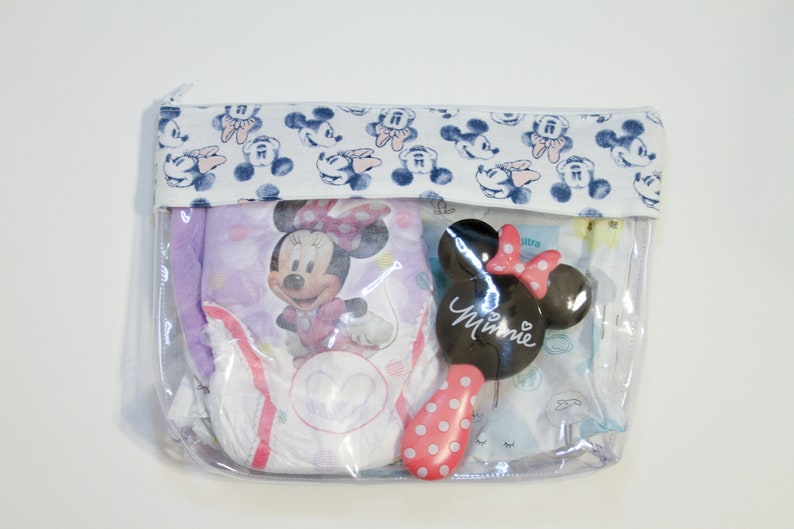 May include: A clear plastic zippered pouch with a white fabric flap featuring a blue and white Mickey Mouse print. The pouch contains a purple and white diaper with a Minnie Mouse design, a white and blue diaper, and a black and pink Minnie Mouse hairbrush.