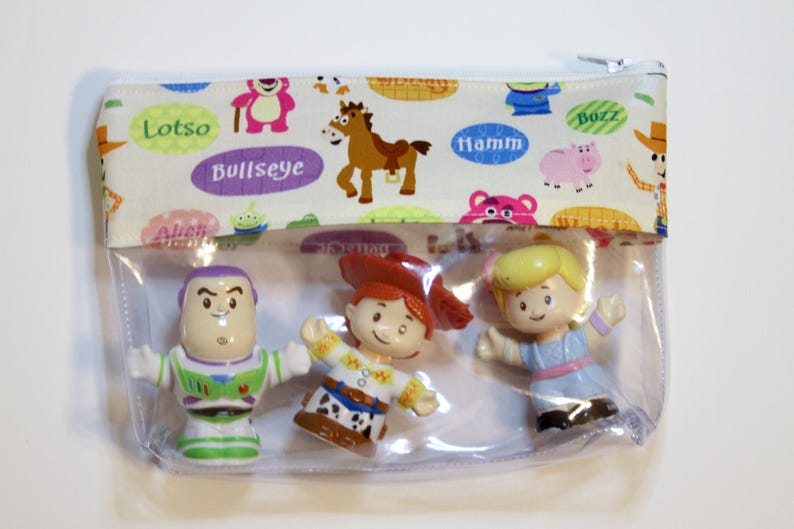 May include: A clear plastic zippered pouch with a white fabric lining featuring Toy Story characters and names like Lotso, Bullseye, Hamm, and Buzz. The pouch contains three small plastic figurines of Woody, Buzz Lightyear, and Jessie.