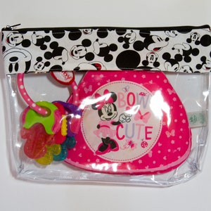 K&ouml;nnte beinhalten: Eine transparente Rei&szlig;verschlusstasche mit einem schwarz-wei&szlig;en Mickey-Mouse-Muster oben. Im Inneren befindet sich ein rosa Babyartikel zum Thema Minnie Mouse und ein farbenfroher Bei&szlig;ring. Der Minnie-Mouse-Artikel tr&auml;gt die Aufschrift "Bow Cute".