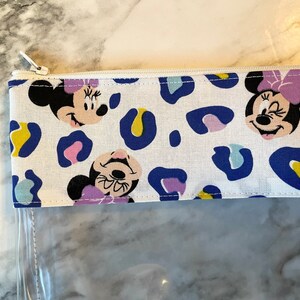 Pode incluir: Uma bolsa branca com z&iacute;per e frente de pl&aacute;stico transparente. A bolsa tem uma estampa de leopardo azul e branco com imagens do Mickey Mouse.