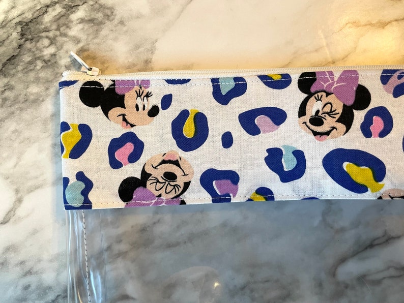 Pode incluir: Uma bolsa branca com z&iacute;per e frente de pl&aacute;stico transparente. A bolsa tem uma estampa de leopardo azul e branco com imagens do Mickey Mouse.