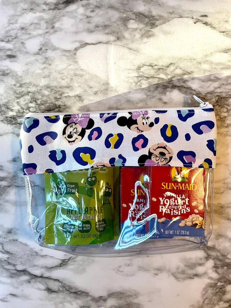 Pode incluir: Uma bolsa transparente com z&iacute;per com fundo branco e padr&atilde;o de leopardo. A bolsa tem dois compartimentos transparentes com dois pacotes de lanches dentro. Um pacote &eacute; verde e diz "From 100 Fruit Hi-Apple Fruit on the Go" e o outro pacote &eacute; vermelho e diz "Sun-Maid Vanilla Yogurt Covered Raisins".