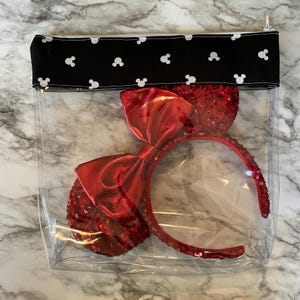 Pu&ograve; includere: Una pochette trasparente in plastica con cerniera e una patta in tessuto nero con silhouette bianche di Topolino. All'interno della pochette c'&egrave; un cerchietto rosso con paillettes e un grande fiocco di raso rosso.