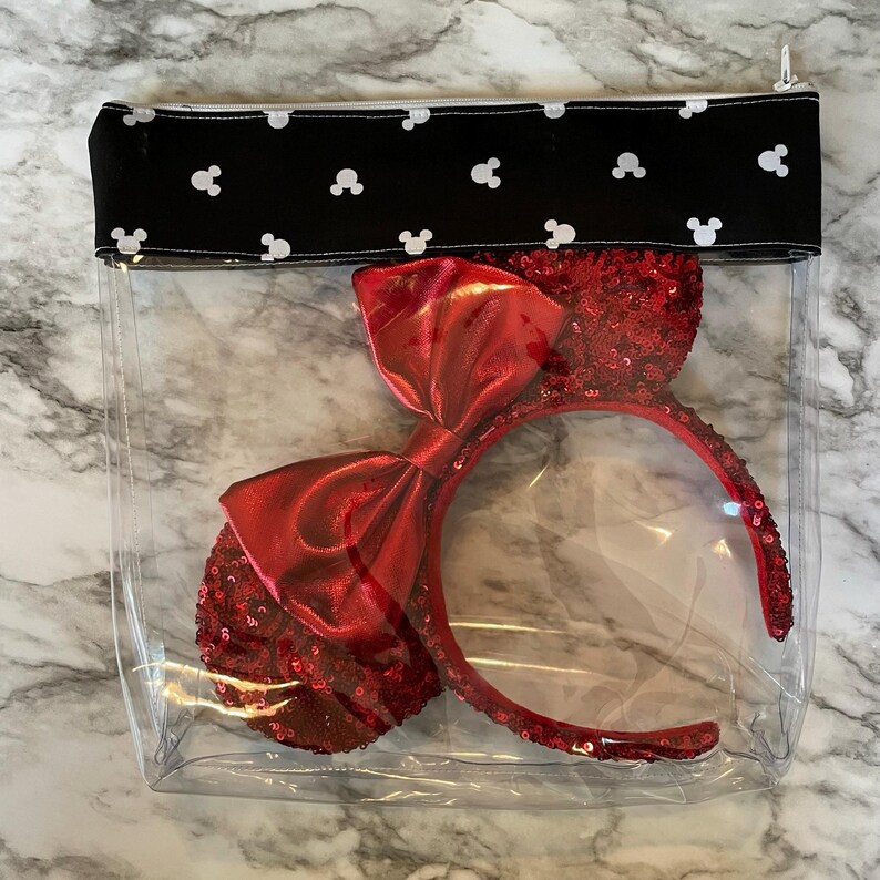 Pu&ograve; includere: Una pochette trasparente in plastica con cerniera e una patta in tessuto nero con silhouette bianche di Topolino. All'interno della pochette c'&egrave; un cerchietto rosso con paillettes e un grande fiocco di raso rosso.
