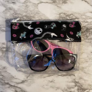 May include: A clear plastic zippered pouch with a black fabric lining featuring a repeating pattern of a character from the Nightmare Before Christmas. The pouch contains two pairs of sunglasses, one pink and one black.