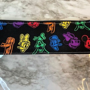 May include: Black pencil case with a zipper closure. The top portion features a repeating pattern of colorful cartoon character faces, including Mickey Mouse, Donald Duck, and Goofy. The bottom half is clear.