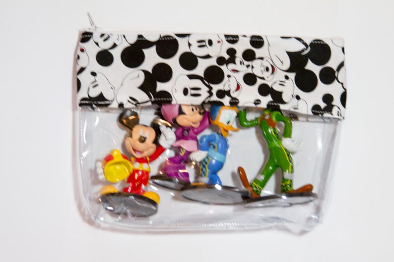 K&ouml;nnte beinhalten: Transparente Rei&szlig;verschlusstasche mit einem schwarz-wei&szlig;en Mickey Mouse-Muster oben. Die Tasche enth&auml;lt Mickey Mouse, Minnie Mouse, Donald Duck und Goofy Figuren. Die farbenfrohen Figuren stehen auf einer transparenten Basis.