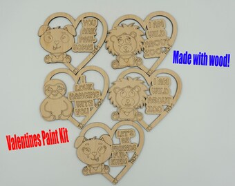 Puede incluir: Un kit de pintura para el Día de San Valentín con recortes de madera en forma de corazón. Cada corazón presenta un diseño de animal y un mensaje como "You are pawsome!" y "I love hanging with you." El kit incluye el texto "Made with wood!" y "Valentines Paint Kit."
