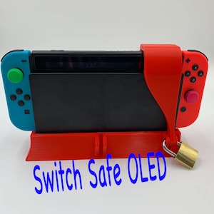 May include: A red and blue Nintendo Switch OLED console is secured in a red 3D printed stand with a padlock and chain. The stand has the text "Switch Safe OLED" printed on the front.