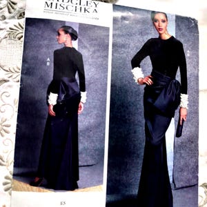 May include: A sewing pattern by Badgley Mischka features a black evening gown with a long skirt and a bow detail. The pattern includes sizes 14-22. The Vogue Patterns designer's name is visible on the pattern.
