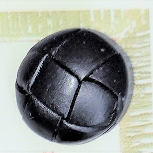 May include: A close-up of a black, round button with a woven or basketweave design. The button is made of a dark material and has a slightly textured surface. The button is likely for clothing or crafts.
