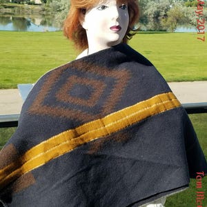 May include: A dark blue and brown patterned blanket with a yellow stripe. The blanket is draped over a mannequin.
