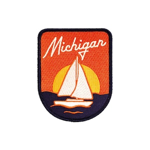 May include: An orange and blue embroidered patch featuring a sailboat and a setting sun. The text "Michigan" is written in white cursive.